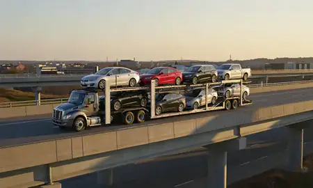 Car transporter with the Auburn, Maine, United States skyline behind it
